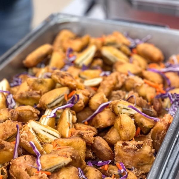 Close-up of golden-fried paneer pakora with shredded purple cabbage and carrots in a metal tray.