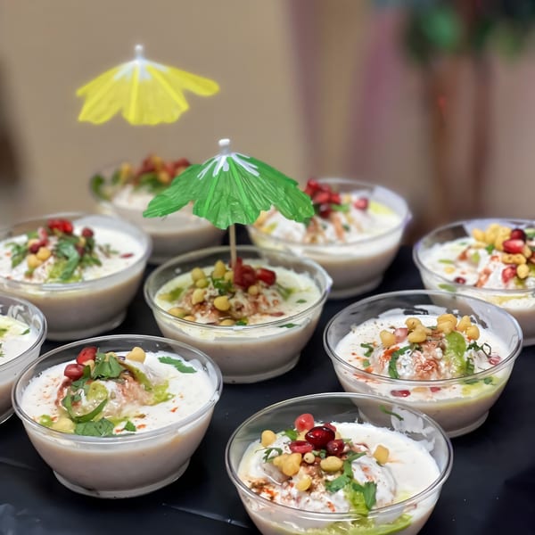 Bowls of Indian dahi bhalla, topped with pomegranate, chickpeas, and green chutney, one with a green umbrella.