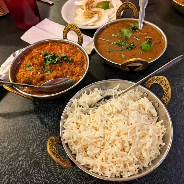Three Indian dishes: two curries with cilantro and a bowl of white rice, served in metal bowls.