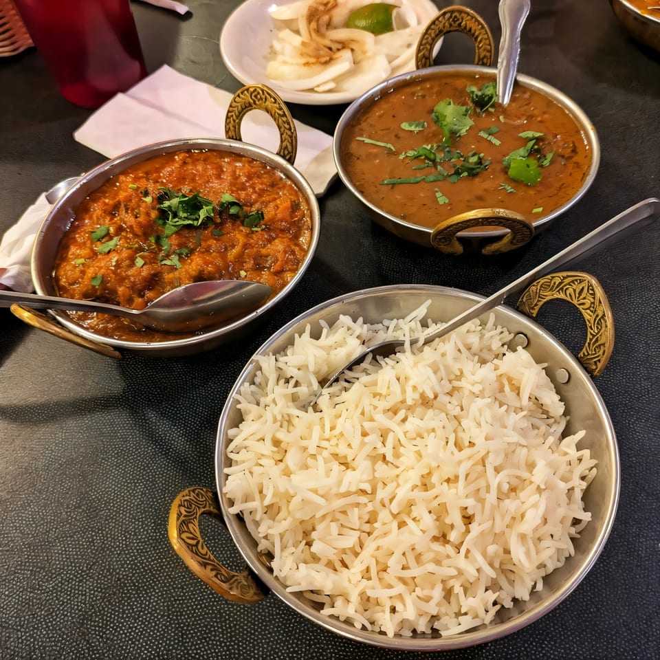 Three Indian dishes: two curries with cilantro and a bowl of white rice, served in metal bowls.