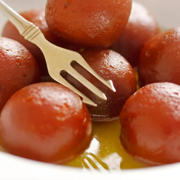Close-up of Gulab Jamun, Indian fried dough balls in syrup, with a fork in a white bowl.
