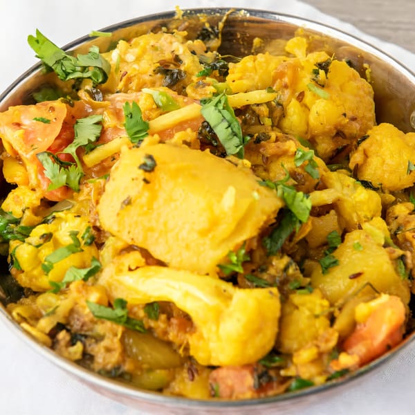 Close-up of Aloo Gobi, an Indian dish with potatoes, cauliflower, tomatoes, and cilantro in a metal bowl.