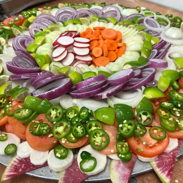 A colorful platter of sliced vegetables, including red onions, carrots, radishes, tomatoes, and jalapeños.