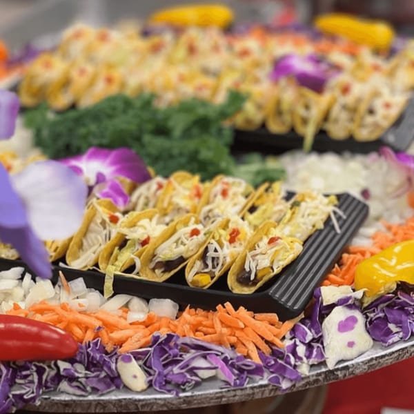Mini tacos with various toppings and fresh shredded vegetables on a large platter.